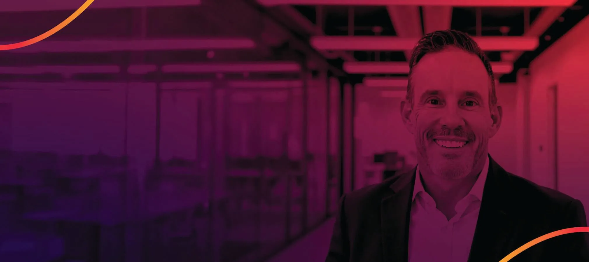 A digitally edited image of a smiling man in a suit, set against a modern office background with glass walls and ceiling lights. The image has a red and purple gradient overlay, with curved orange design elements in the corners, creating a sleek and professional aesthetic.