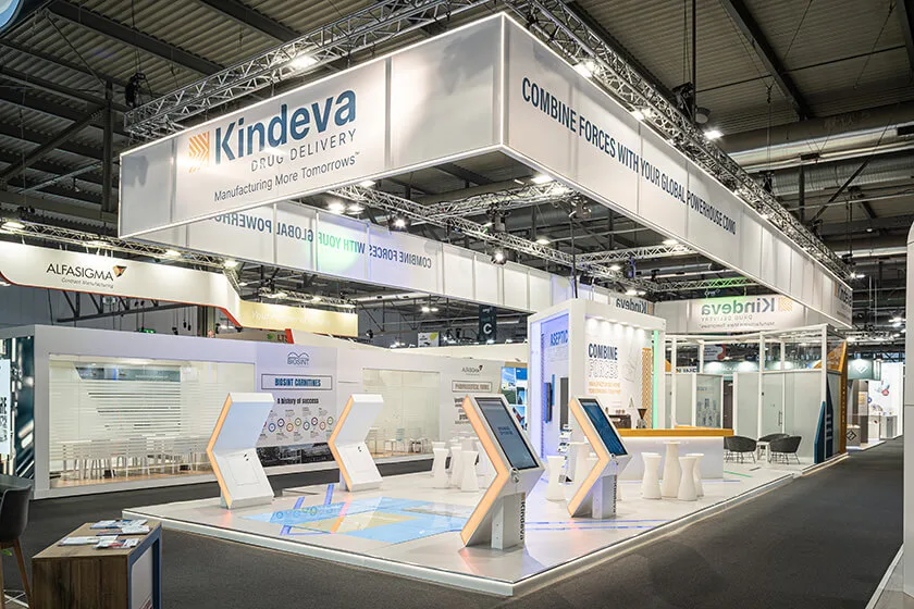Photo of a Kindeva Drug Delivery trade show booth with prominent signage, interactive displays, and branded visuals, set in a large exhibition hall.