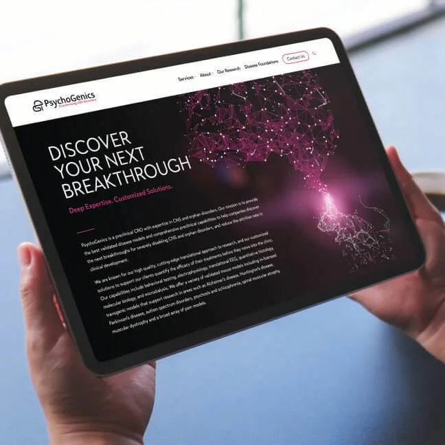 A person holding a tablet displaying the PsychoGenics website. The screen features a dark-themed design with the text 'DISCOVER YOUR NEXT BREAKTHROUGH' in bold white letters, followed by 'Deep Expertise. Customized Solutions.' in pink. A glowing, interconnected neural network graphic in pink and purple is visible on the right side. The website's navigation bar is at the top, showing options like Services, About, and Our Research.