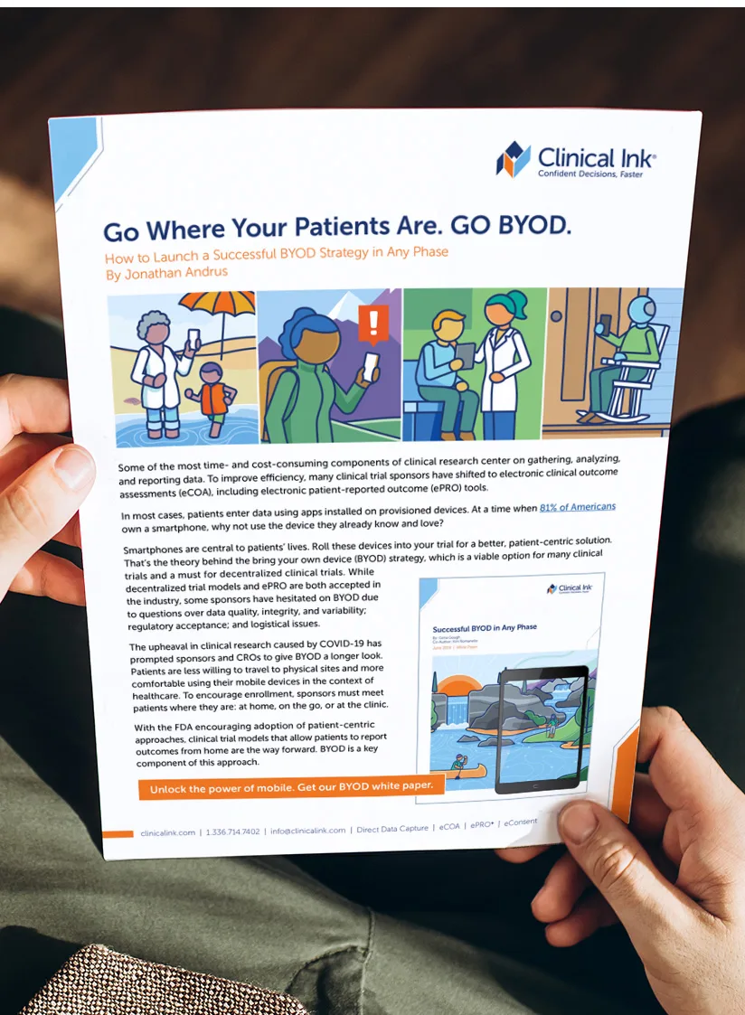 A close-up of someone’s hands holding a printed white paper from Clinical Ink. The top right bears the Clinical Ink logo and tagline “Confident Decisions, Faster.” Centered at the top is the bold headline “Go Where Your Patients Are. GO BYOD.” with the subheading “How to Launch a Successful BYOD Strategy in Any Phase – By Jonathan Andrus.” Directly below is a row of four flat-style illustrations: an older adult and child wading at the beach with a smartphone, a hiker holding up a phone with an alert icon, a clinician and patient reviewing a laptop, and a wheelchair user checking a phone. Underneath, several paragraphs describe how sponsors can use patients’ own mobile devices for electronic outcome reporting (eCOA/ePRO) in clinical trials. To the right is a small inset graphic of a tablet displaying a kayaker on the water. At the bottom, an orange banner proclaims “Unlock the power of mobile. Get our BYOD white paper.” The footer lists contact details and services (Direct Data Capture, eCOA, ePRO, eConsent).