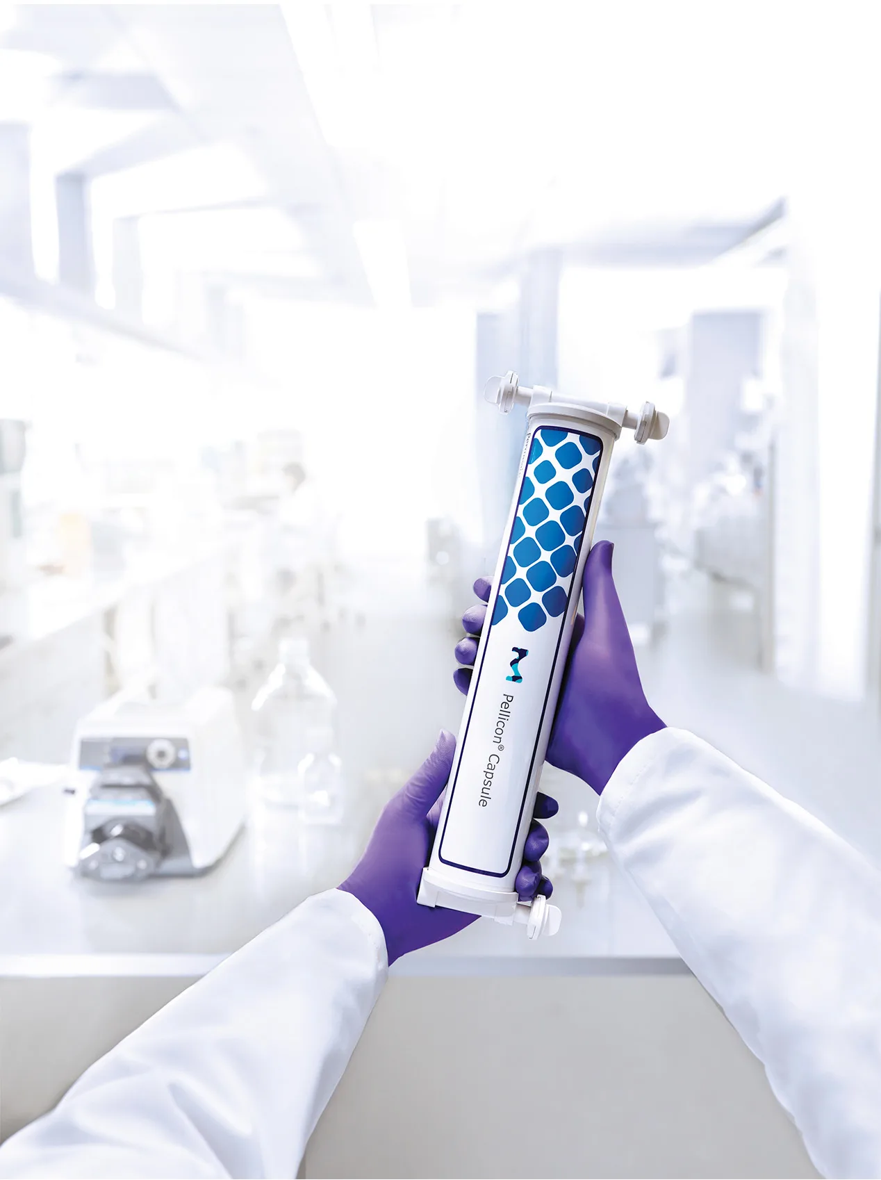 Arms wearing a white lab coat and purple gloves holding a MilliporeSigma Pellicon® Capsule device in a bright, modern laboratory setting, with scientific equipment and glassware visible in the background.