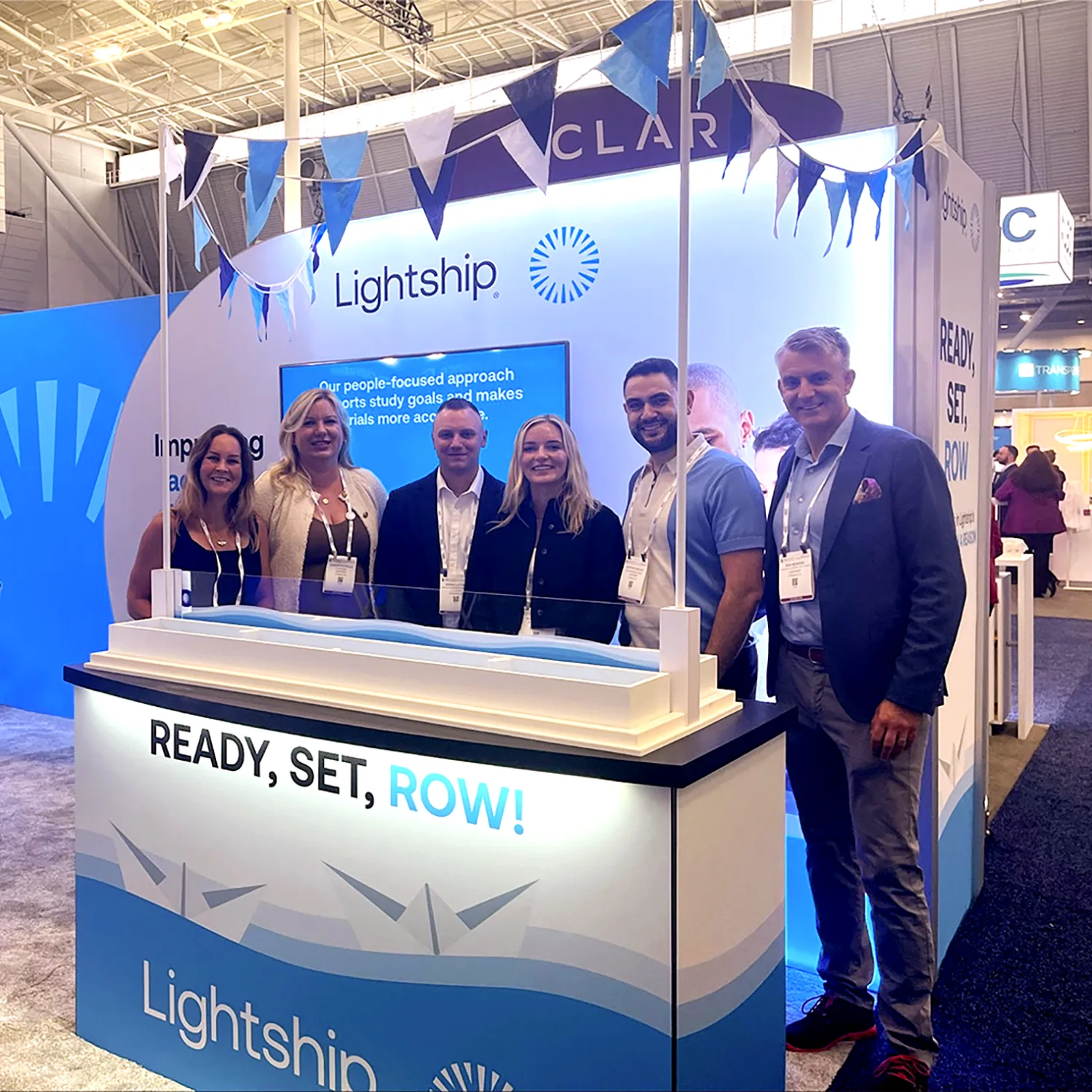 Group of six people standing at the Lightship trade show booth featuring blue and white branding, banners, and a READY SET ROW slogan, showcasing life science marketing at an industry event.