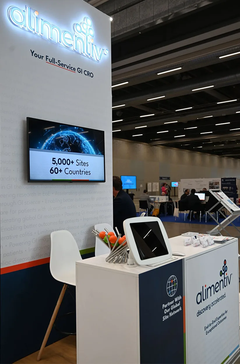 Conference booth counter with Alimentiv branding digital screen showing global site network statistics and informational materials on display
