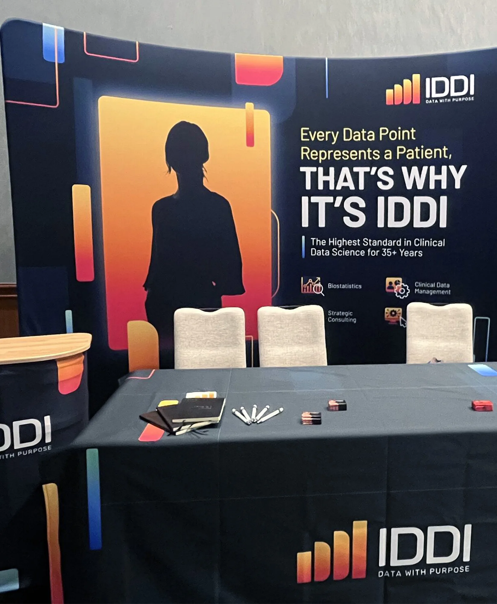 Trade show booth with IDDI branding featuring large backdrop graphics table with notebooks pens and promotional materials