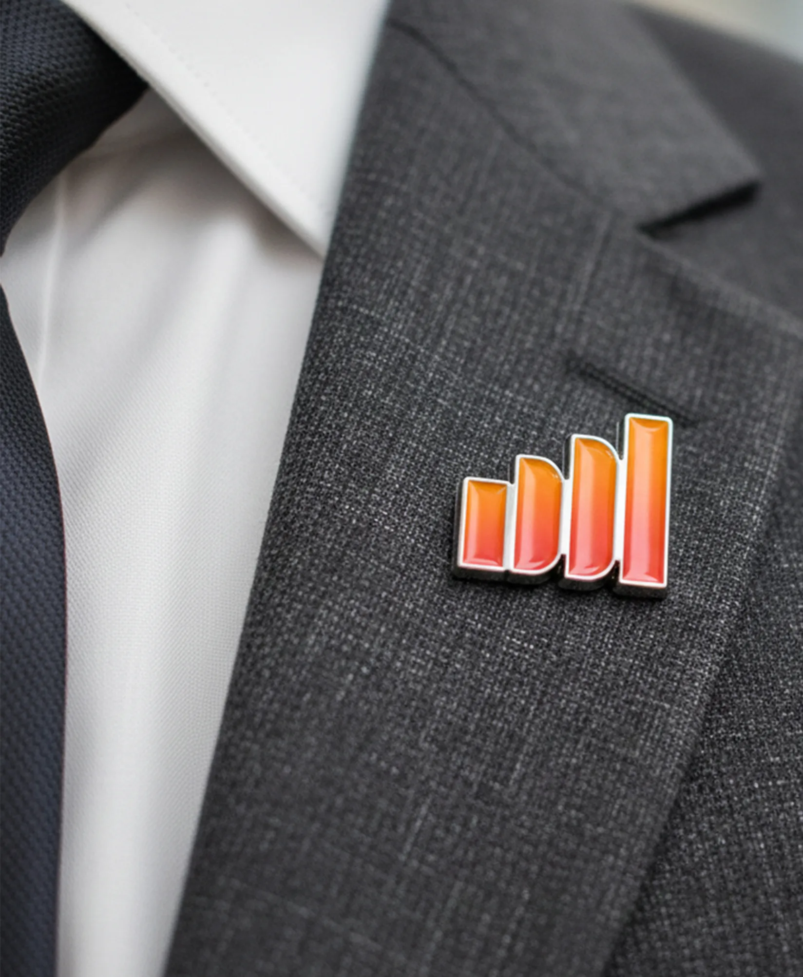 Close up of IDDI enamel pin on a gray suit lapel showing gradient bar logo