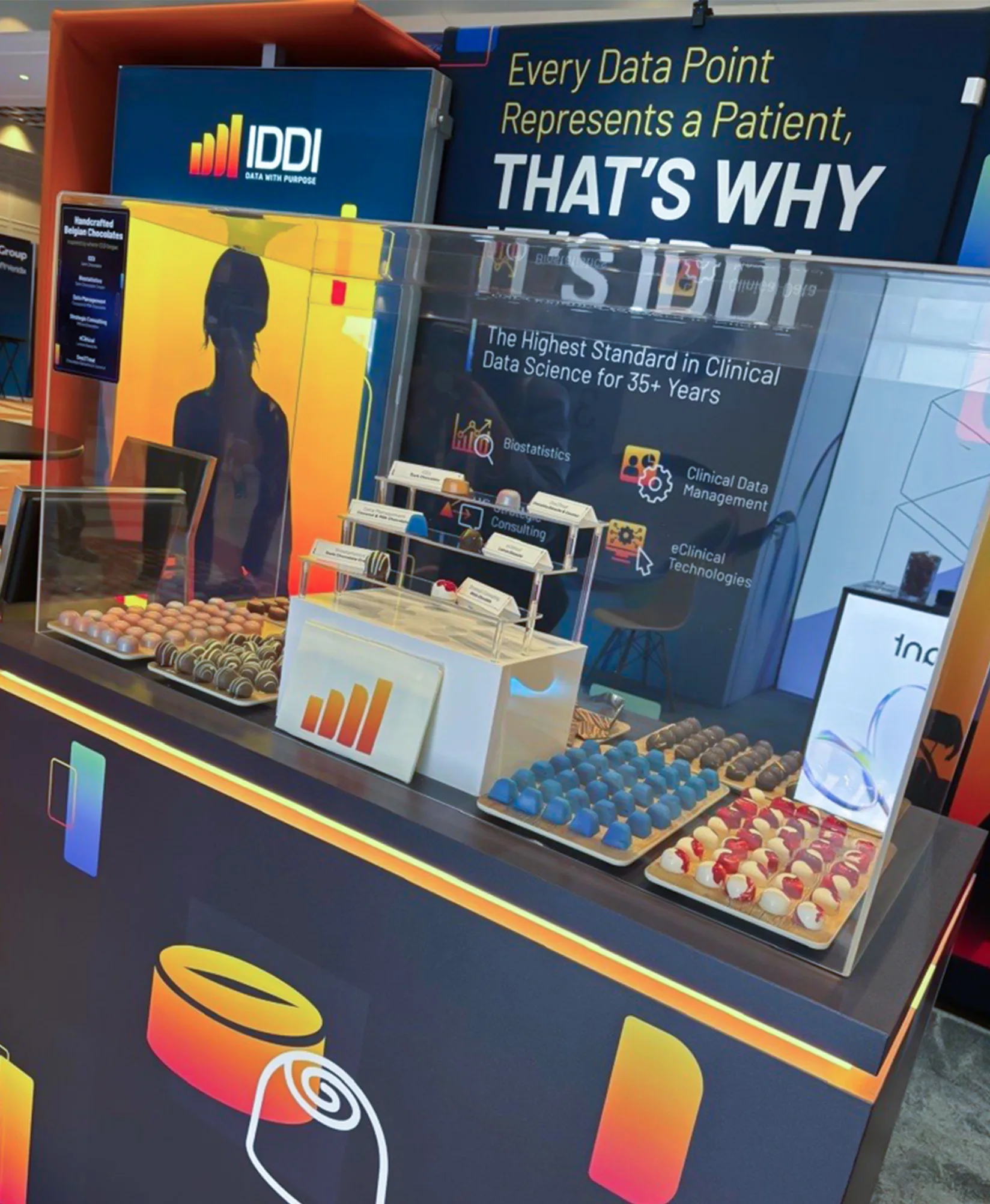 Trade show booth display with IDDI branding chocolates and product samples on counter with signage in background