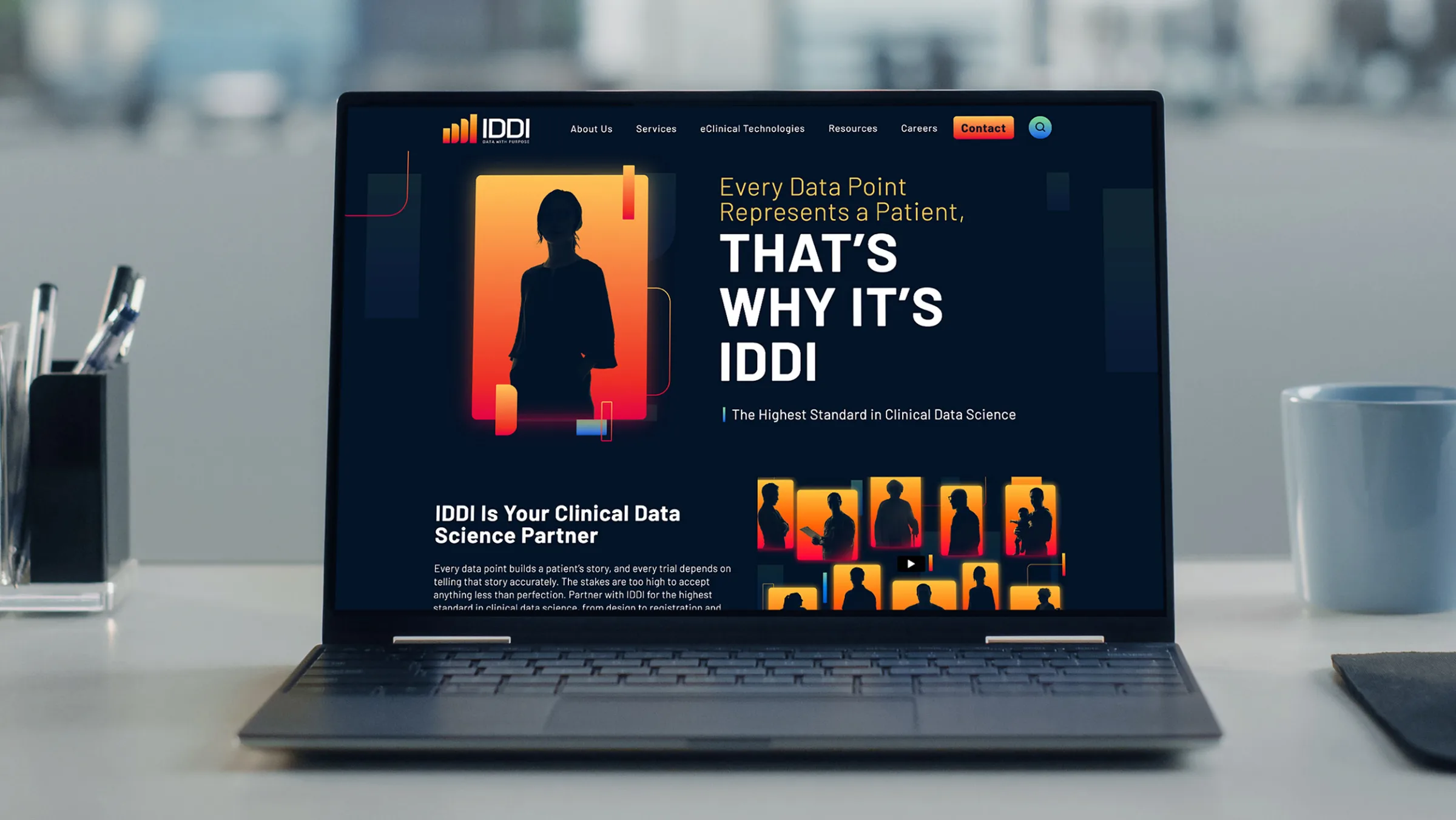 Laptop on a desk displaying the IDDI website homepage with the headline "Every Data Point Represents a Patient, That's Why It's IDDI."